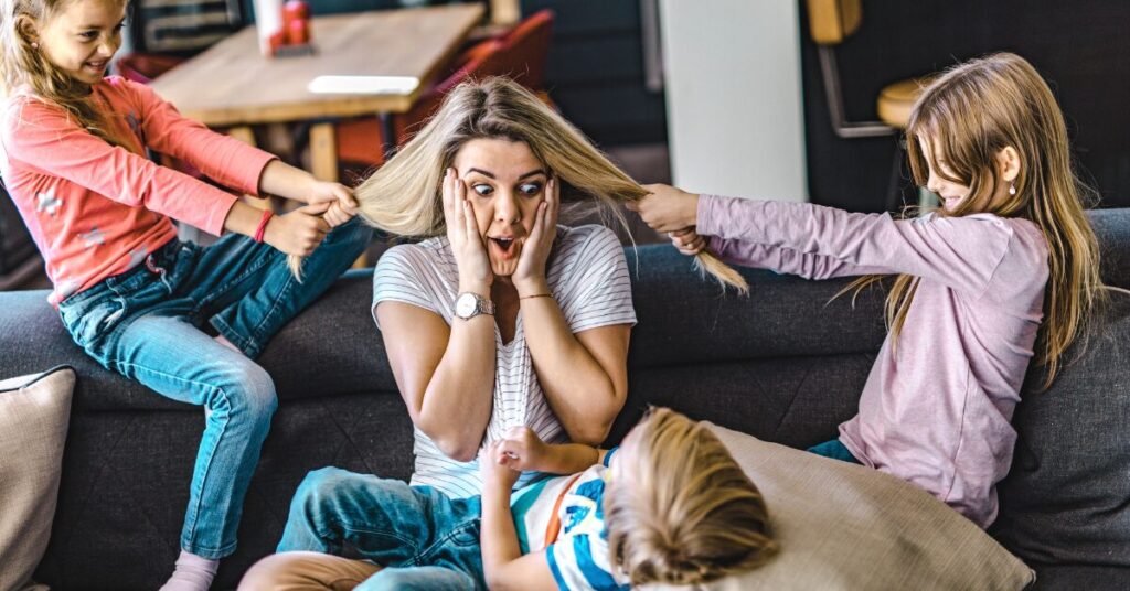 parent holding face looking exasperated as two children pull on her hair from either side of her