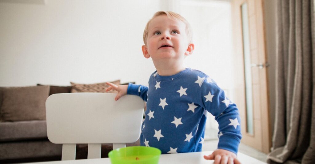 distract young caucasian child in pajamas appearing distracted from his food in a bowl on a table by something in the environment we cannot see