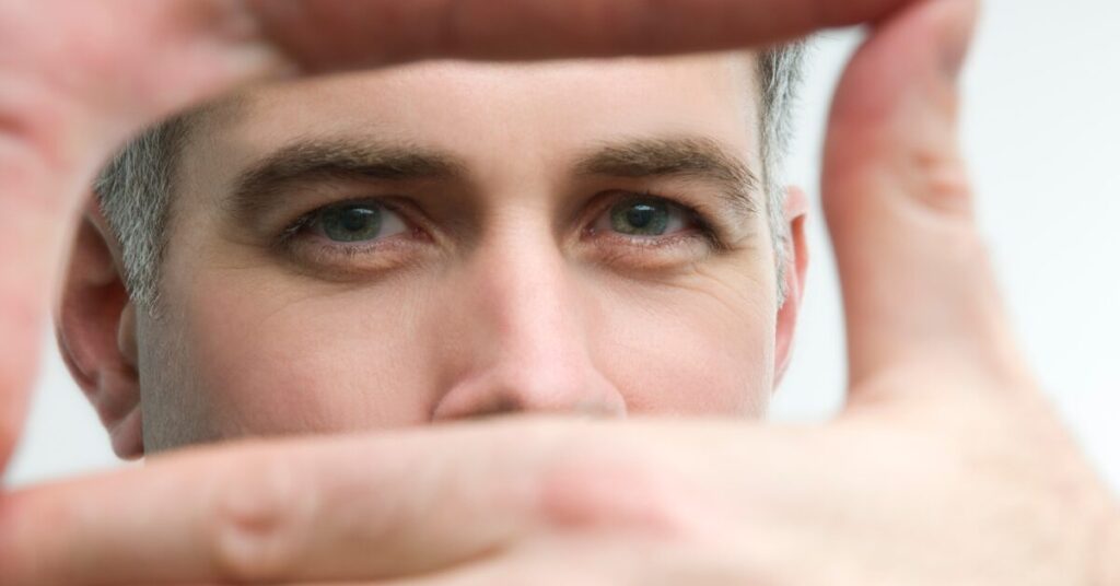 focusing caucasian male looking at camera with his hands connected like a director framing a shot. he is focusing.