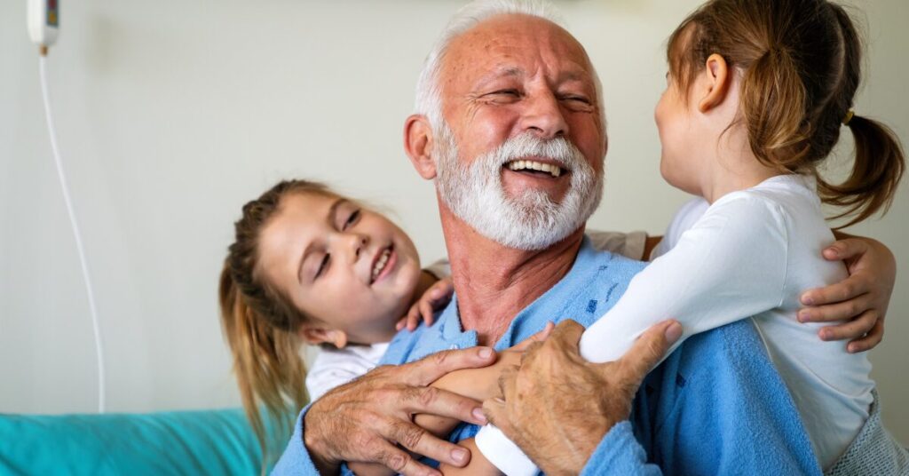 an older man with two young kids hugging him as he smiles and they smile